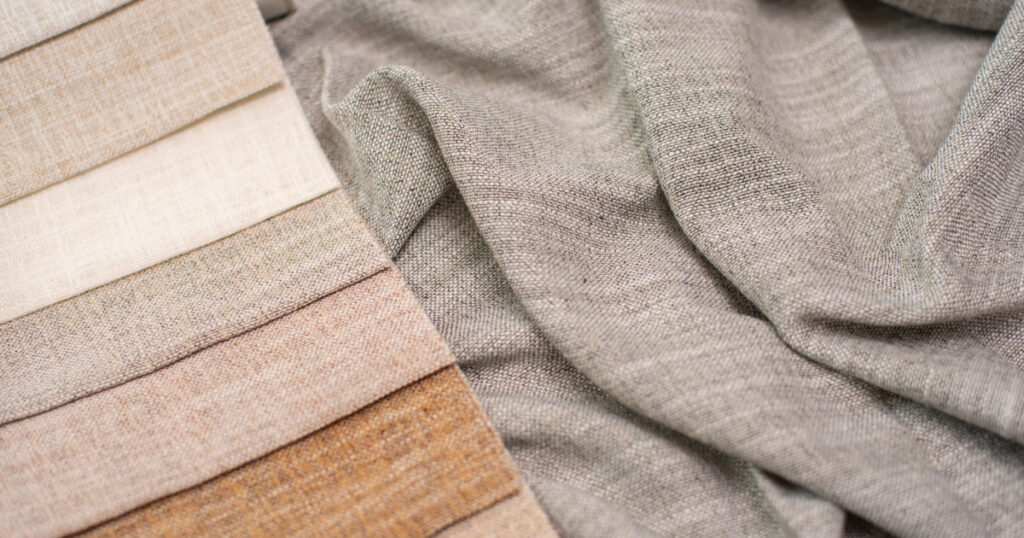 A close-up of natural fabric swatches in earthy tones, including beige, cream, and brown, alongside a loosely draped gray fabric.