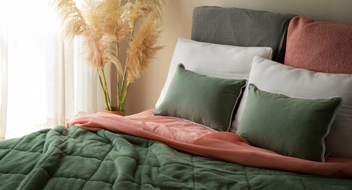 A green and pink bedroom setting with a bed, pillows, and a vase of dried flowers.