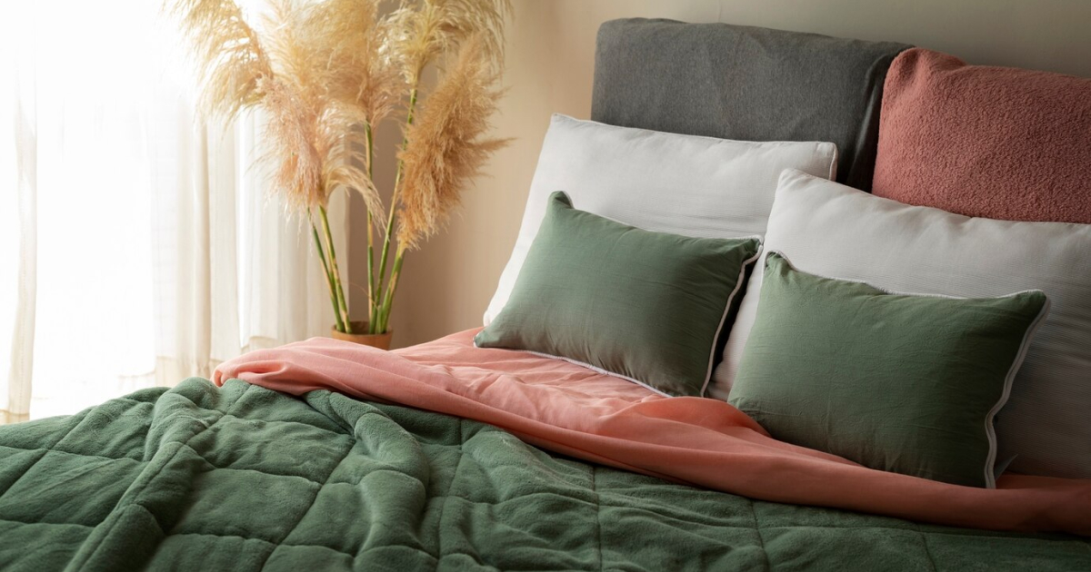 A green and pink bedroom setting with a bed, pillows, and a vase of dried flowers.